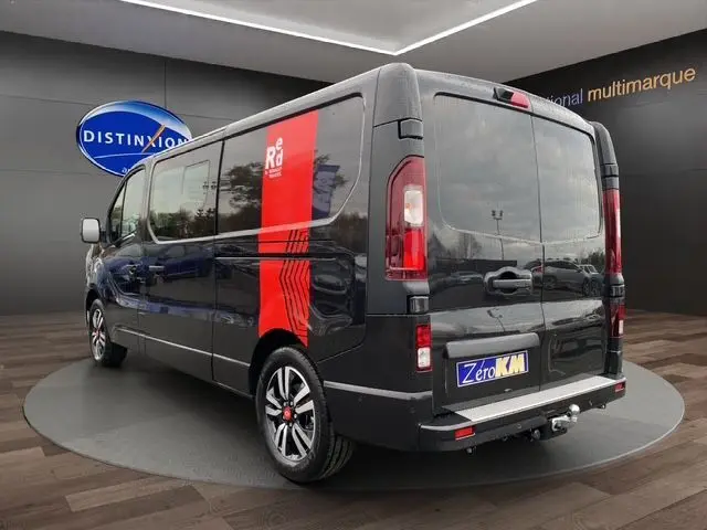 Vue 3/4 arrière droite du Renault Trafic cabine approfondie noir avec jantes alu noires, barres de toit et attelage visible.