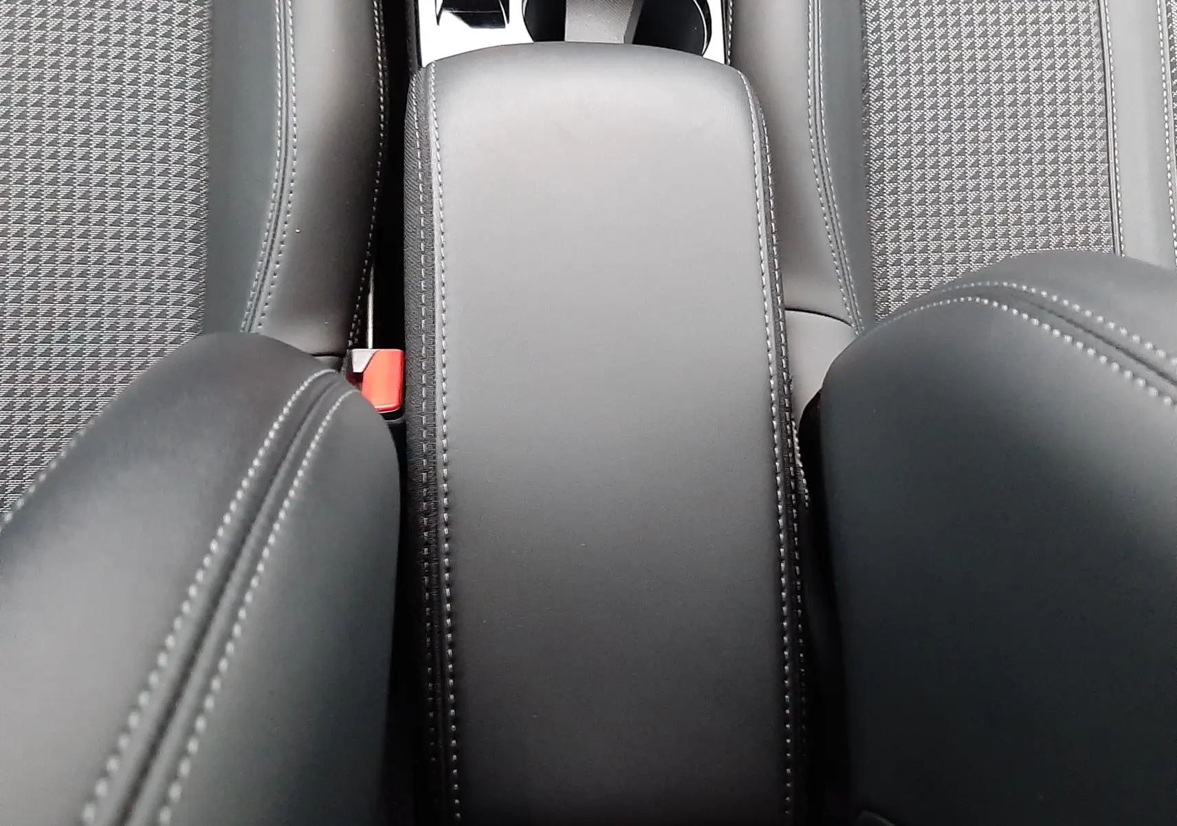 Vue rapprochée de l'accoudoir central en cuir noir et des sièges avant en tissu gris du Peugeot 2008 2023.