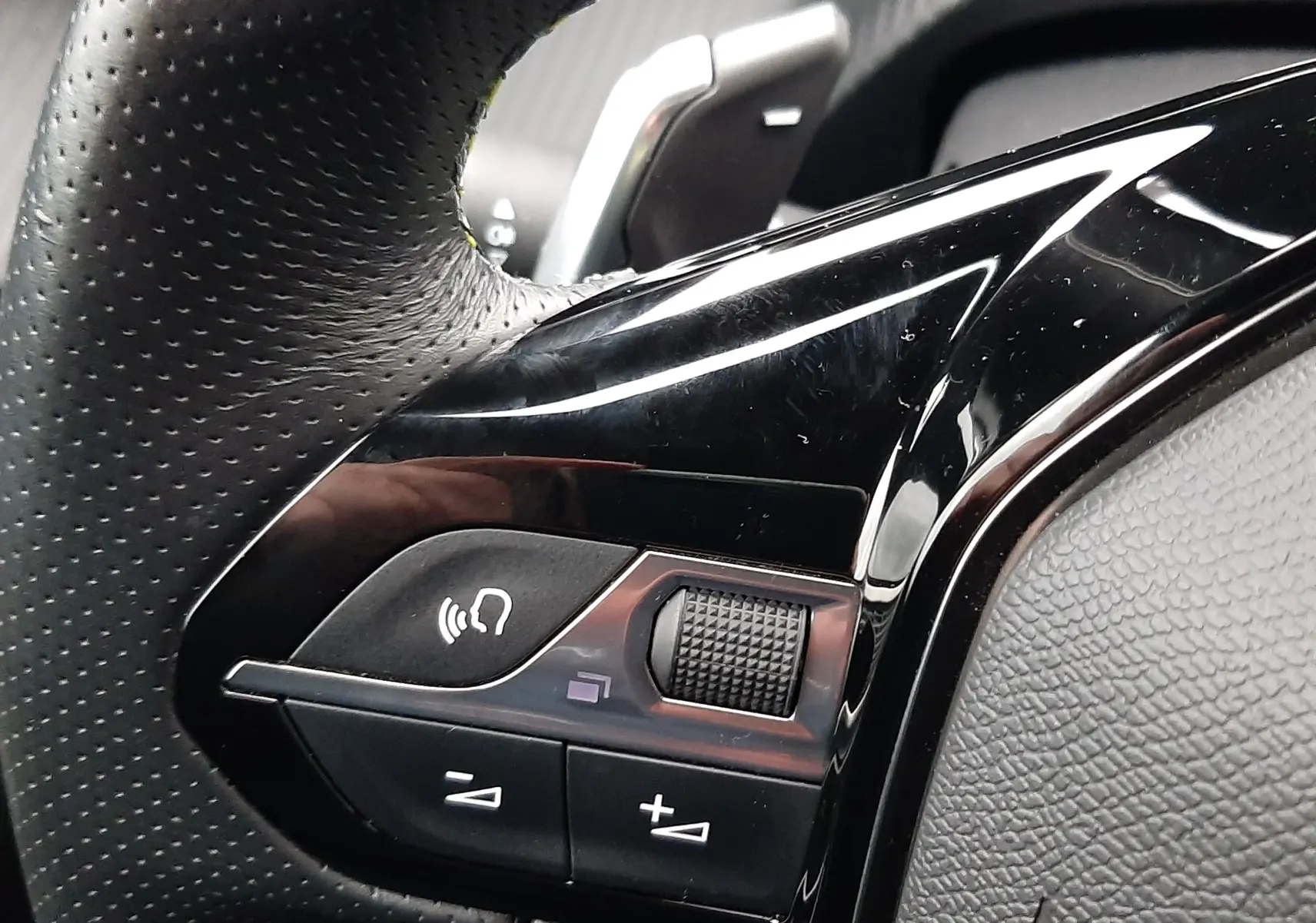 Gros plan sur les commandes gauche du volant en cuir perforé du Peugeot 2008 blanc nacré 2023 avec palettes de changement de vitesse.