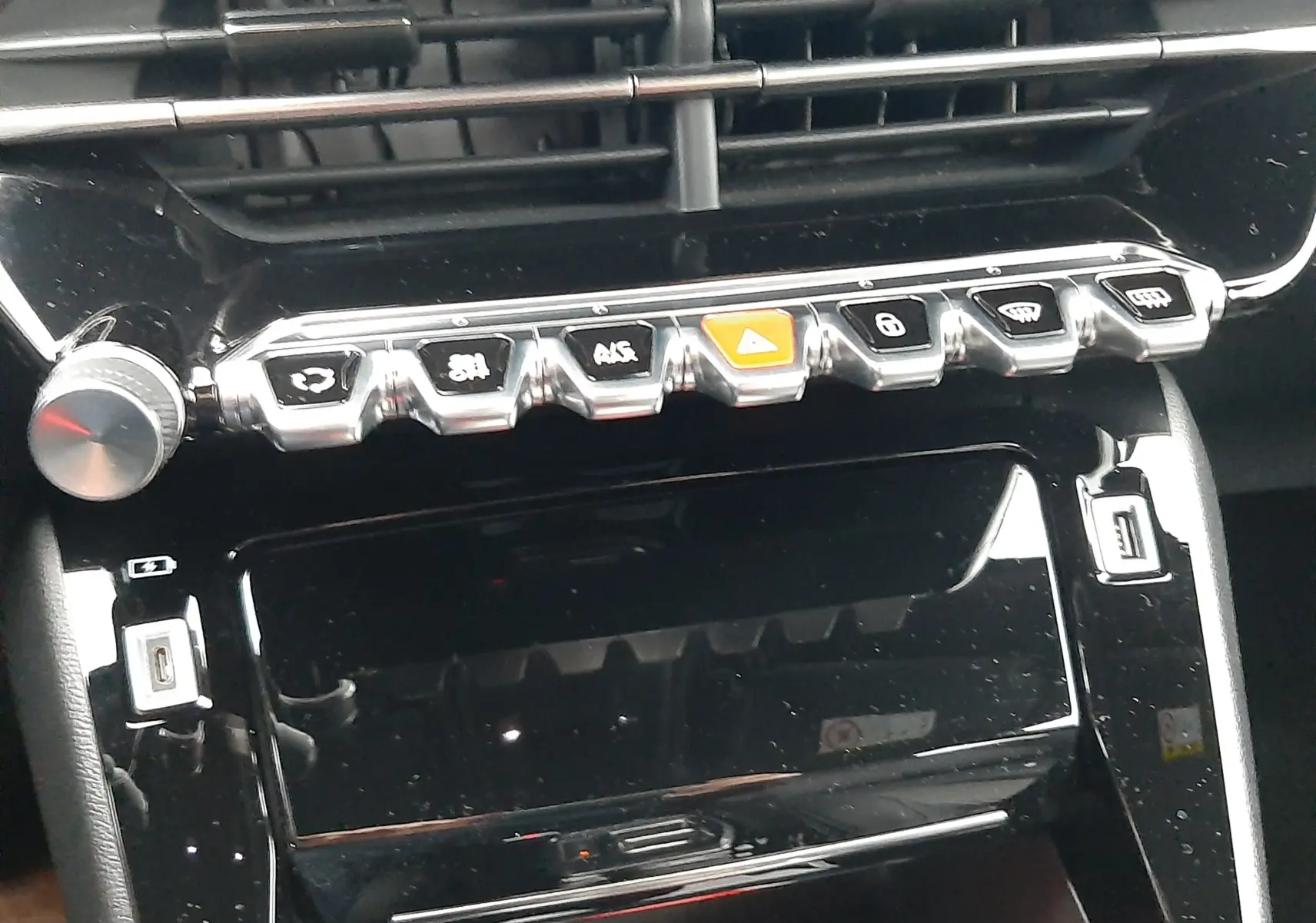 Vue rapprochée du tableau de bord noir brillant du Peugeot 2008 2023, mettant en valeur les commandes chromées et les aérateurs.