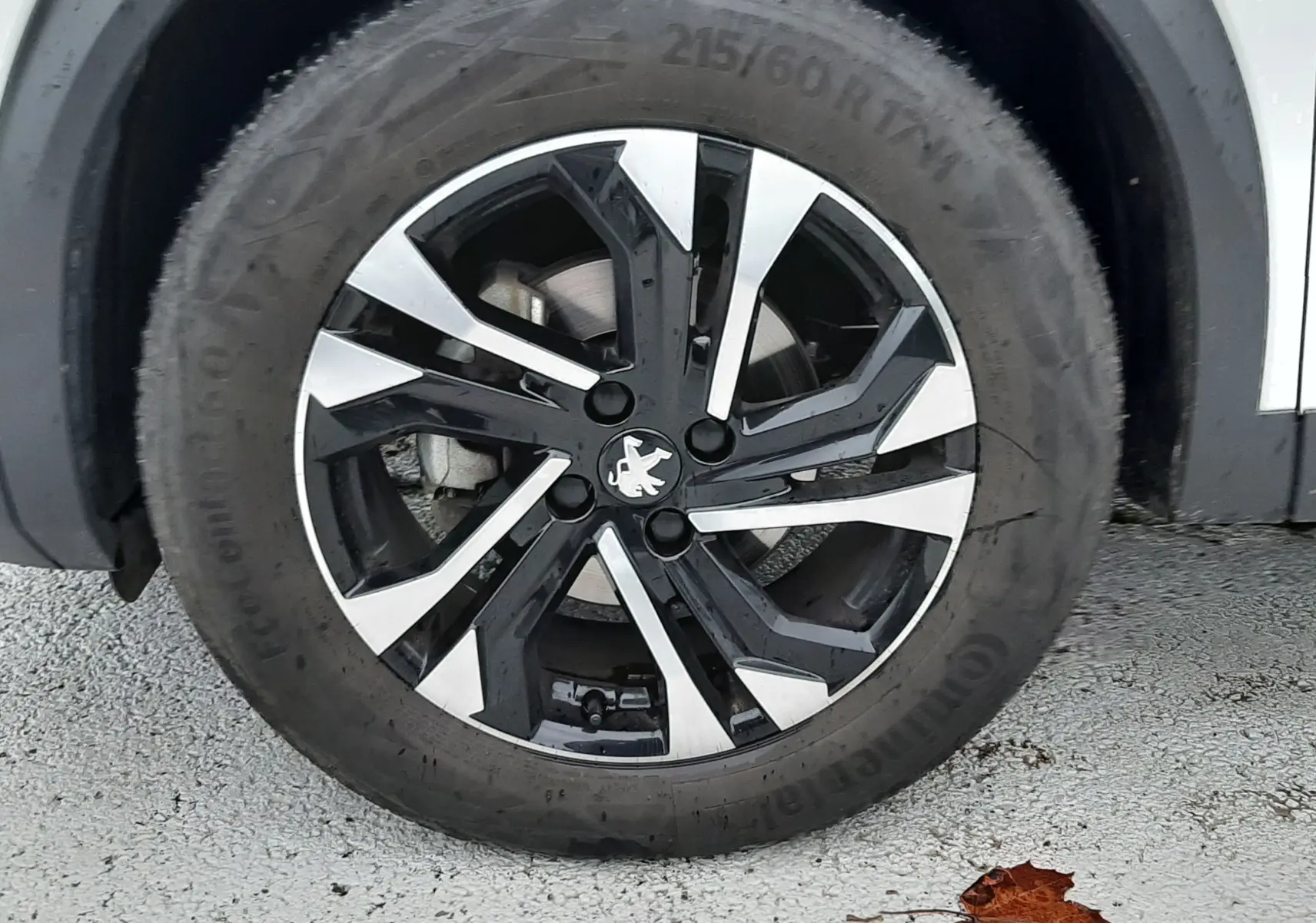 Gros plan sur la jante noire et argentée du Peugeot 2008 blanc nacré avec logo lion au centre.