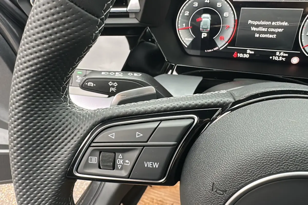 Gros plan sur le volant cuir à méplat et les commandes multifonctions de l'Audi A3 TFSI 150 Hybrid S-Line 2025.