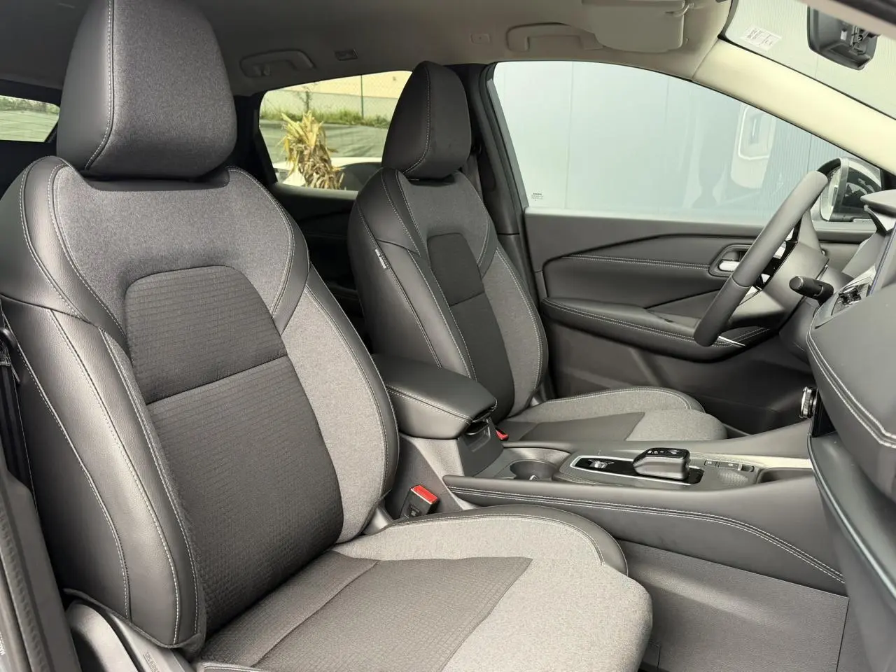 Vue intérieure côté droit du Nissan Qashqai 2025, sièges avant bi-matière gris et noir avec console centrale moderne.