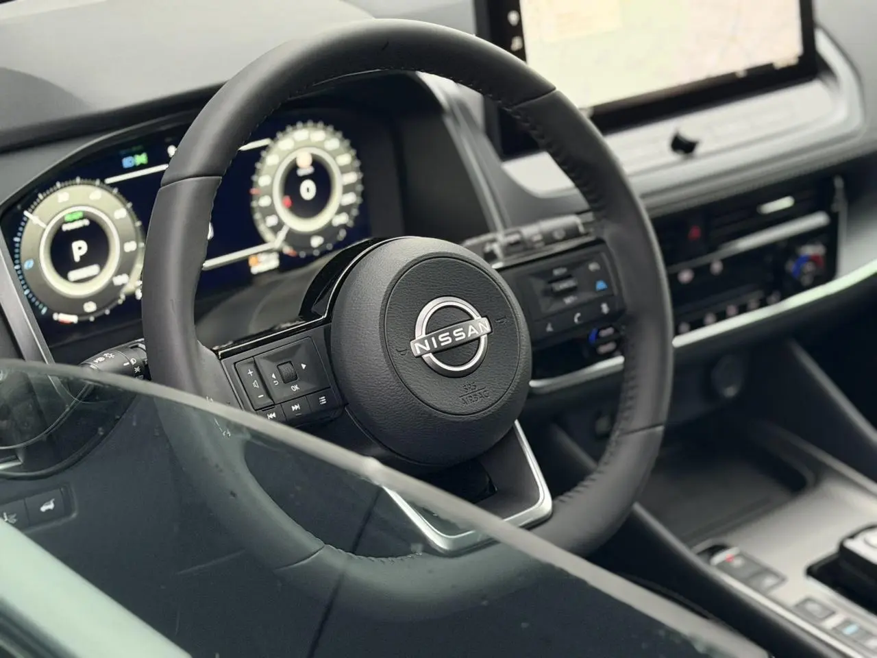 Vue intérieure rapprochée du volant noir et du tableau de bord numérique du Nissan Qashqai III e-Power gris Squale.