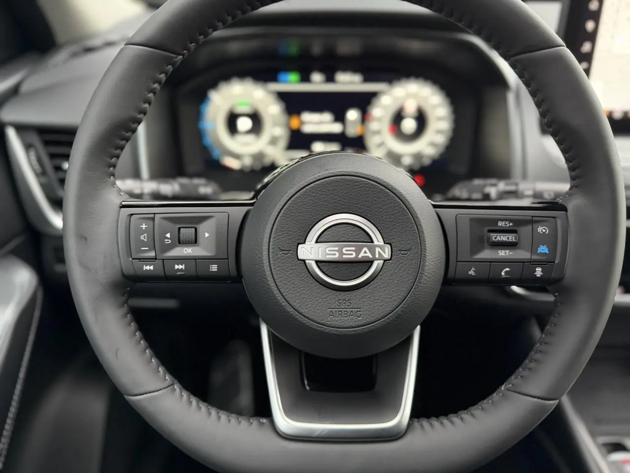 Vue rapprochée du volant cuir noir du Nissan Qashqai 2025 avec commandes intégrées et tableau de bord numérique flou.