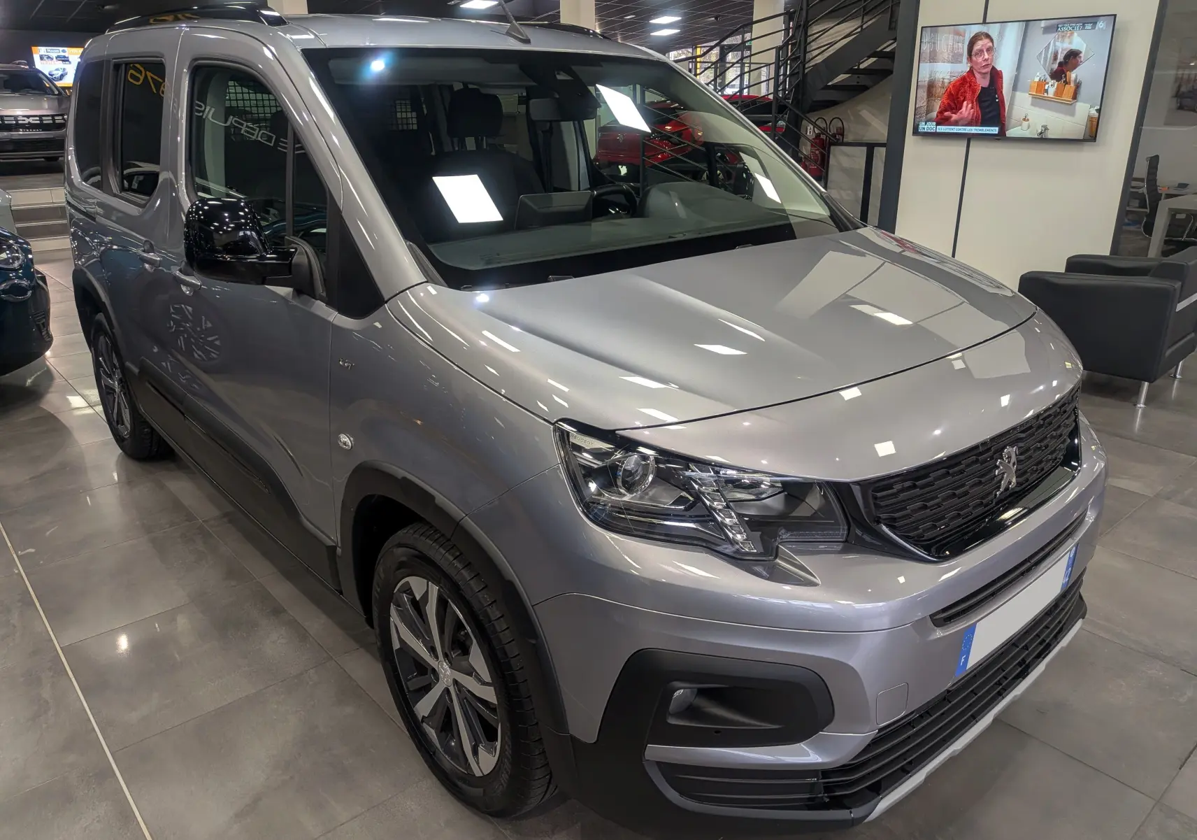 Peugeot Rifter gris Artense en 3/4 avant droit, avec calandre noire et jantes alliage bicolores visibles en showroom.