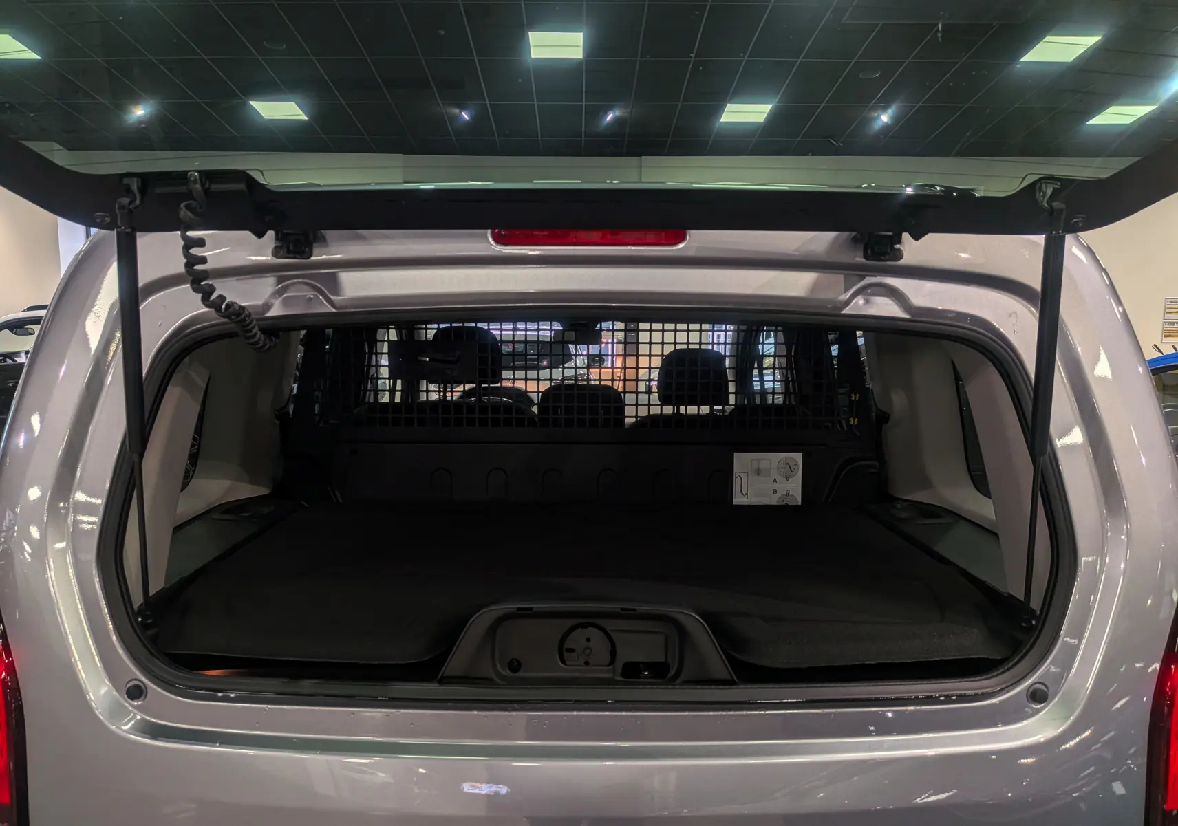 Vue arrière du coffre ouvert du Peugeot Rifter BlueHDi 130 Gris Artense, avec séparation grillagée visible à l'intérieur.