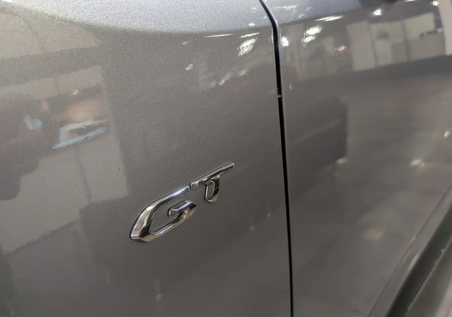 Gros plan sur l’inscription GT en chrome sur la porte gris Artense d’un Peugeot Rifter 2024.