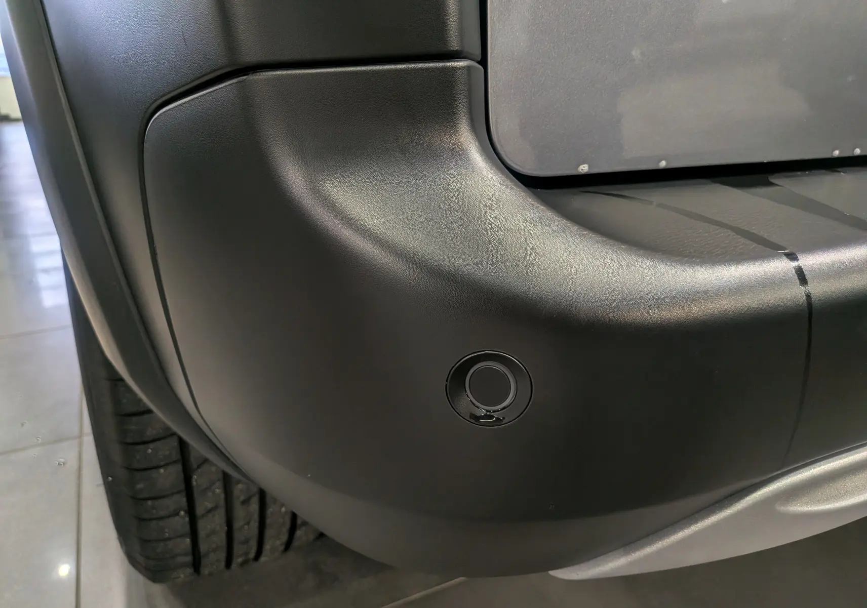 Détail du pare-chocs arrière gauche gris Artense du Peugeot Rifter 2024 avec capteur de stationnement visible.