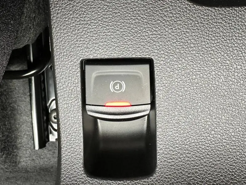 Gros plan sur le bouton de frein de stationnement électrique rouge dans l'habitacle du Dacia Jogger noir nacré.