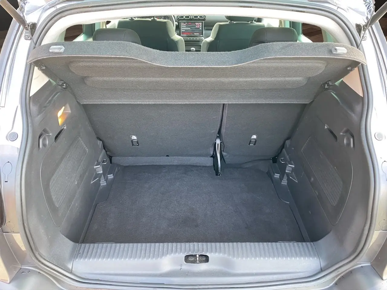 Coffre ouvert vu de l’arrière d’une Citroën C3 Aircross gris platinium avec intérieur sombre et tablette de coffre relevée.