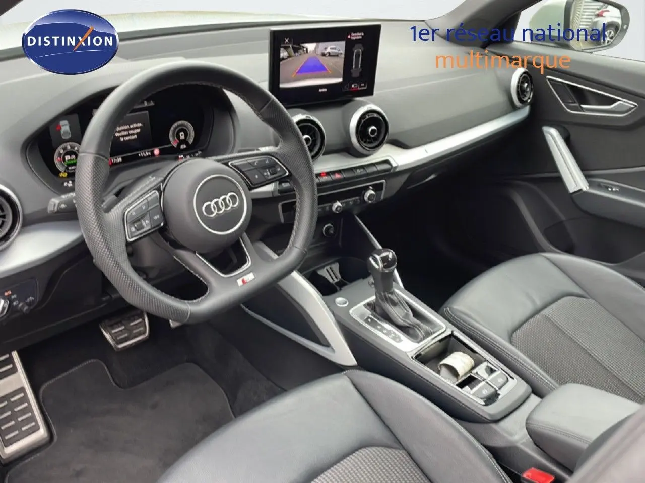 Vue intérieure côté conducteur de l'Audi Q2 2025, avec volant cuir, console centrale et écran multimédia affichant la caméra de recul.