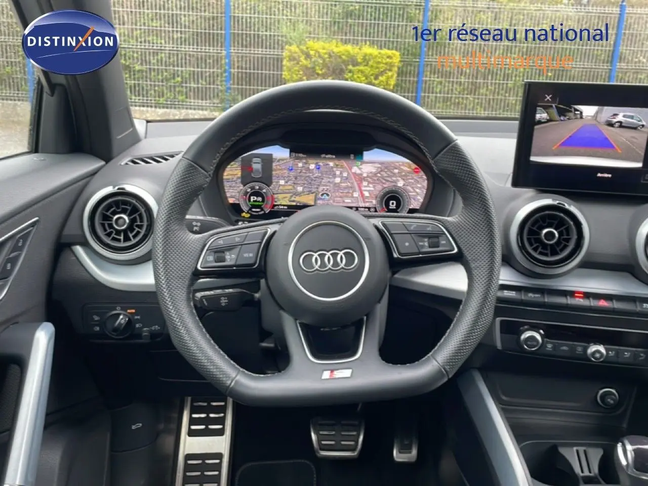 Vue intérieure centrée sur le volant Audi S-Line avec tableau de bord digital et écran de caméra de recul.