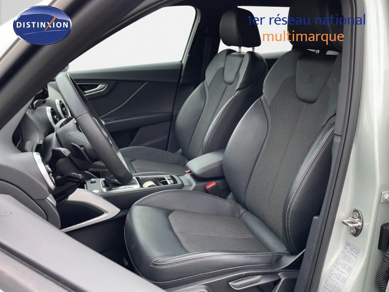 Vue intérieure côté conducteur de l'Audi Q2 argent rose métal 2025, sièges sport cuir noir avec logo S-Line embossé.