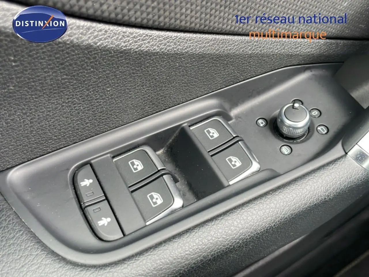 Gros plan sur les commandes de lève-vitres et réglage des rétroviseurs côté conducteur d’un Audi Q2 argent rose métal.