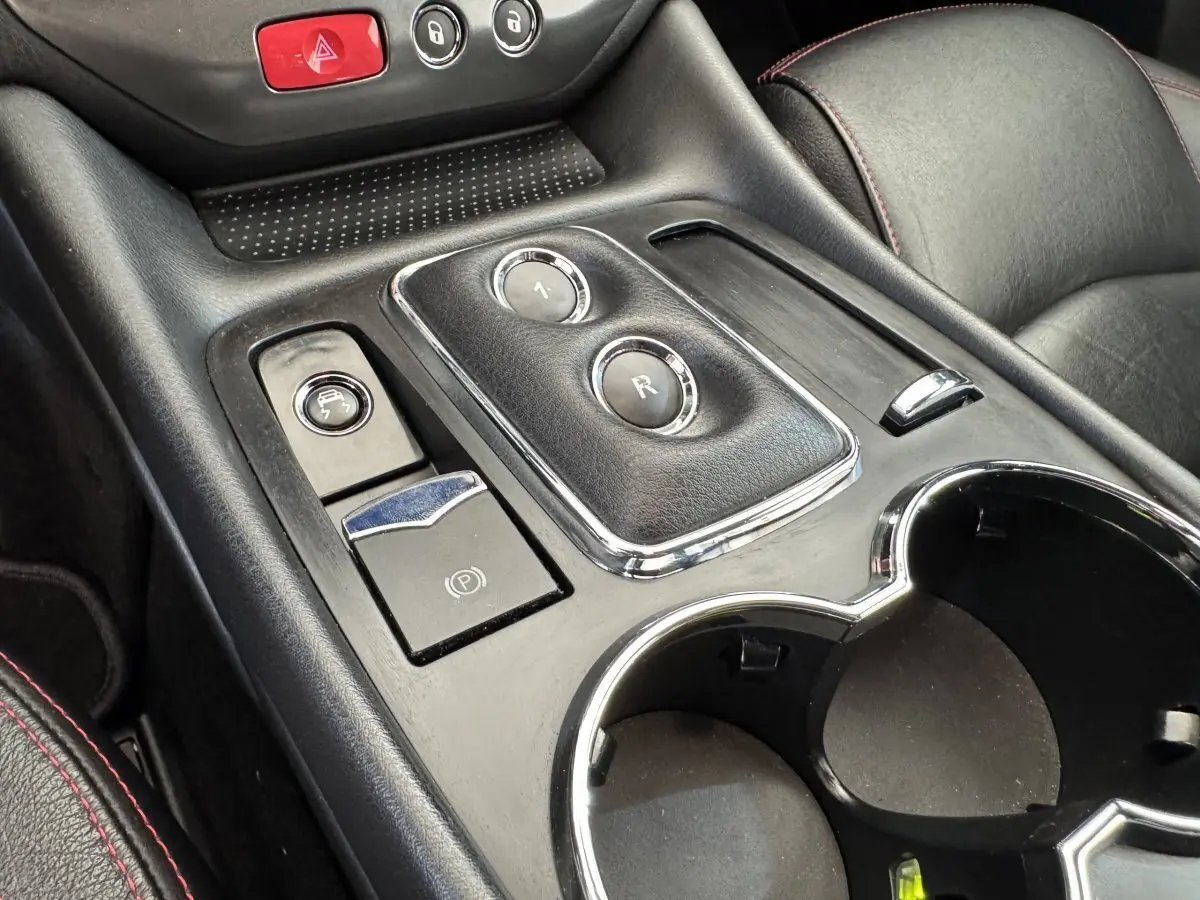 Gros plan sur la console centrale noire de la Maserati Granturismo S 4.7 2010, avec boutons de boîte auto et porte-gobelets.
