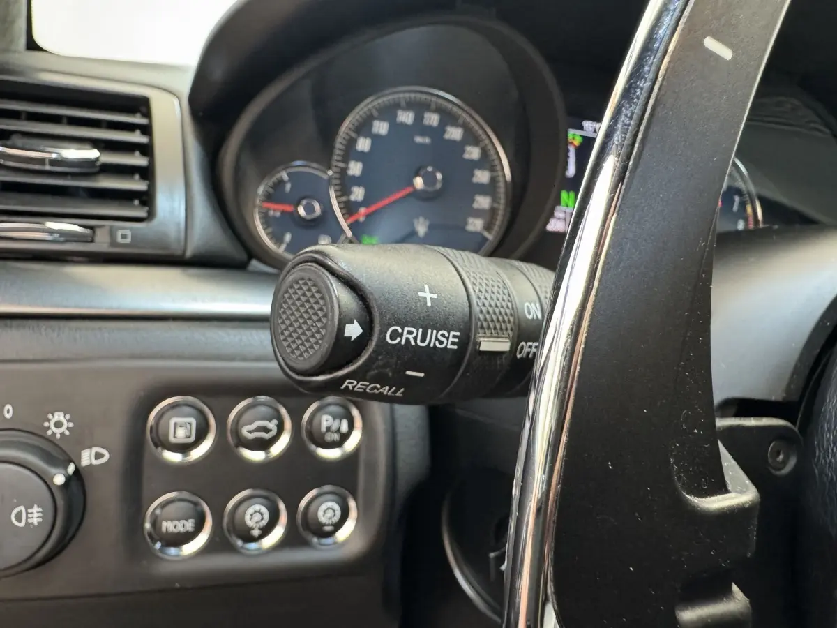 Gros plan sur le volant et commandes du régulateur de vitesse d’une Maserati Granturismo S 4.7 gris foncé, tableau de bord visible.