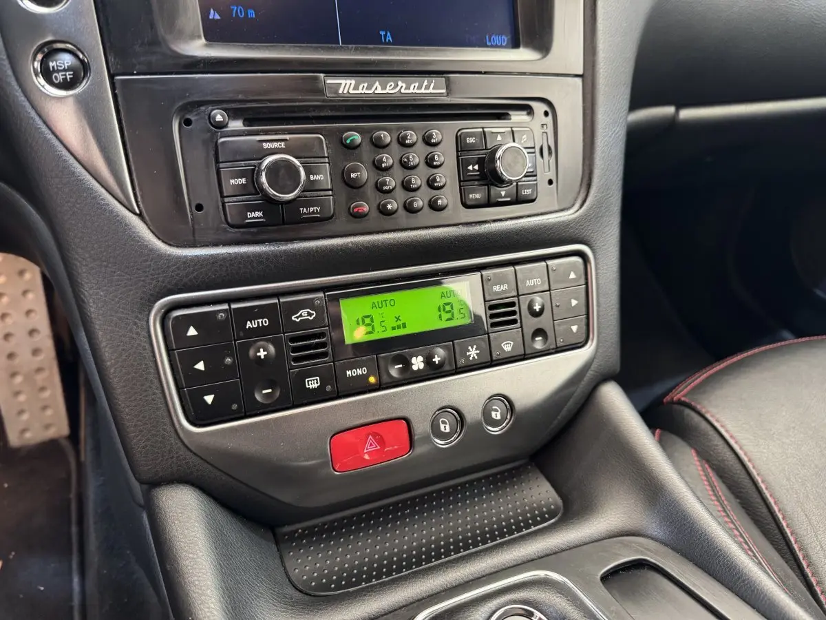 Vue rapprochée de la console centrale noire de la Maserati Granturismo S 4.7 2010 avec commandes climatisation et radio.