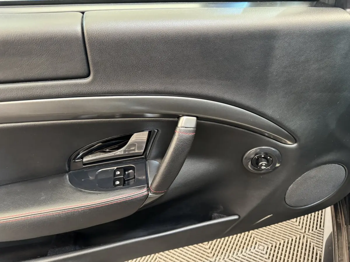 Vue rapprochée de la porte intérieure côté gauche d'une Maserati Granturismo S 4.7 gris foncé avec surpiqûres rouges.