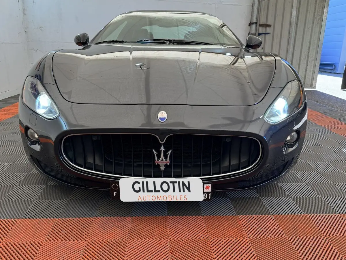 Vue avant rapprochée d'une Maserati Granturismo S 4.7 gris foncé avec phares allumés et calandre imposante.