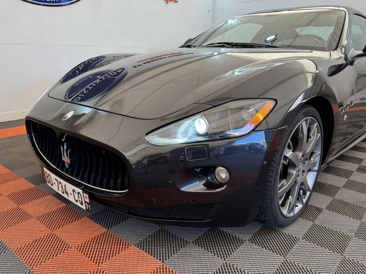 Vue 3/4 avant droit d'une Maserati Granturismo S 4.7 gris foncé avec phares bi-xénon allumés et jantes alliage.