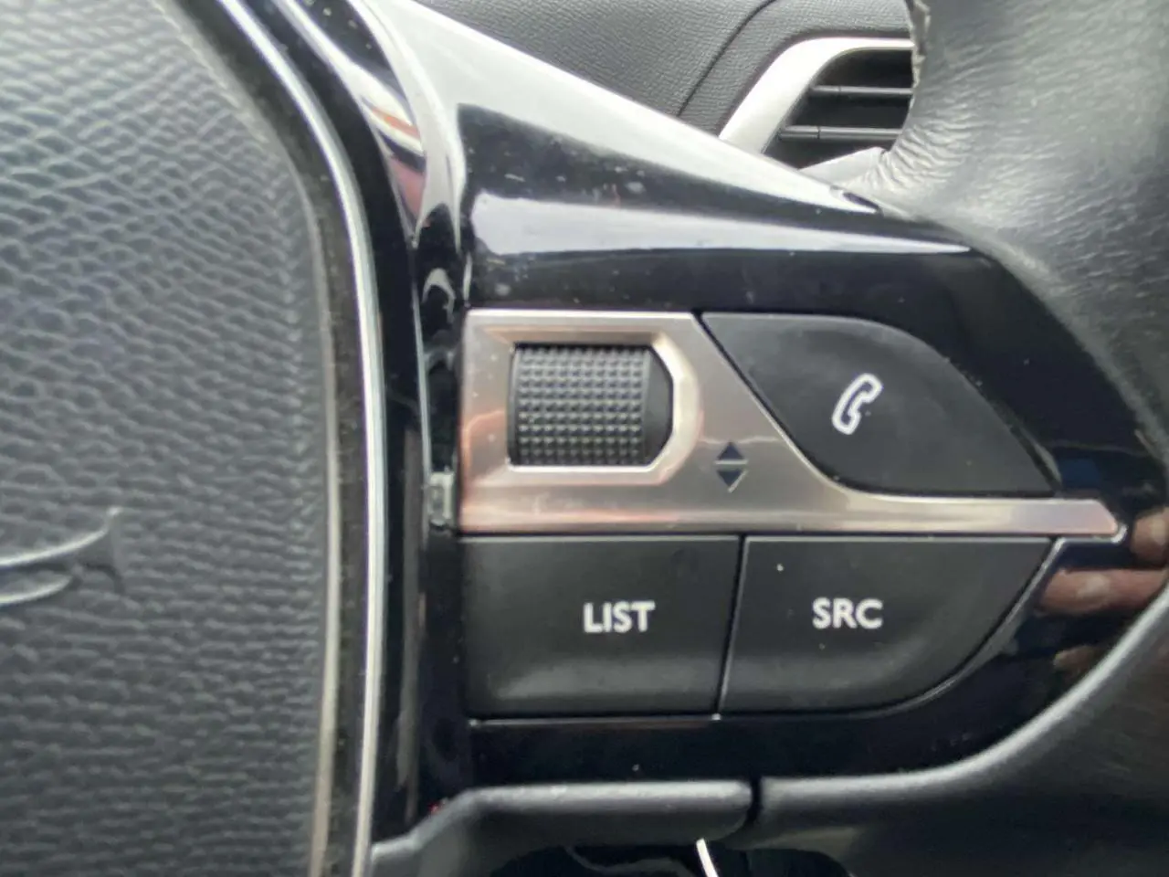 Gros plan sur les commandes du volant noir du Peugeot 3008, boutons LIST et SRC visibles.
