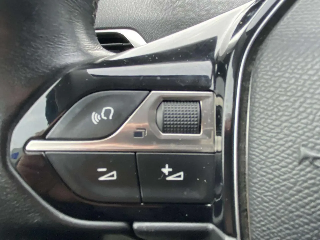 Gros plan sur les commandes de volume au volant du Peugeot 3008, finition noire brillante et cuir texturé.