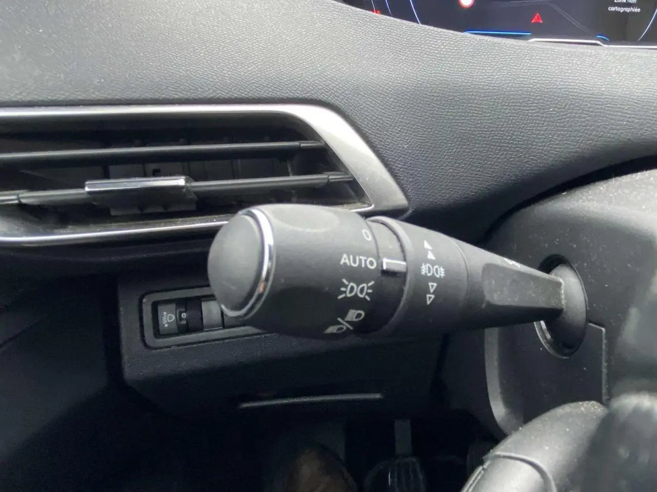 Gros plan sur la commande d’éclairage à gauche du volant dans l’habitacle du Peugeot 3008 marron foncé.