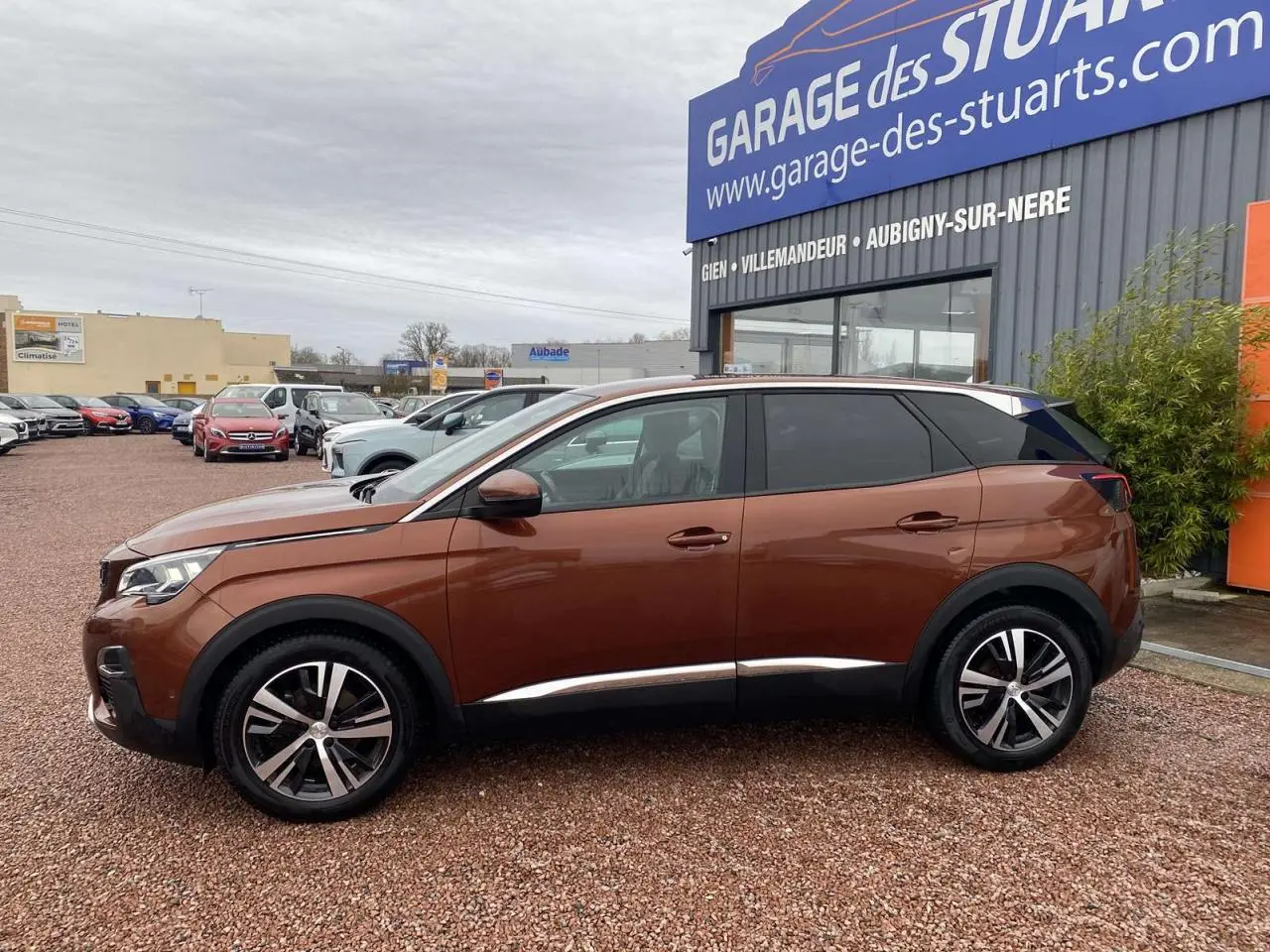 Vue de profil côté gauche d’un Peugeot 3008 marron foncé avec jantes alliage 18 pouces, stationné devant un garage.
