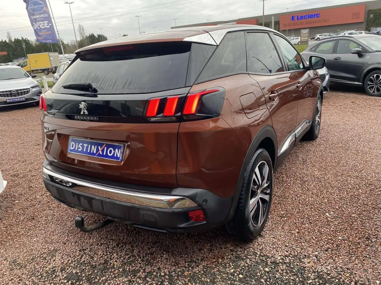 Vue 3/4 arrière droite d'un Peugeot 3008 marron foncé avec attelage et jantes alliage 18 pouces sur parking.