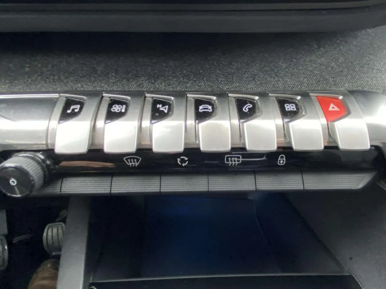 Gros plan sur la rangée de boutons de commande argentés et rouge du tableau de bord du Peugeot 3008 marron foncé.
