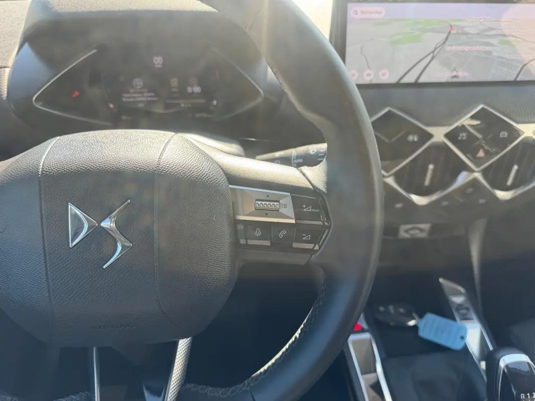 Vue rapprochée du volant DS d’une DS3 2024 gris, avec commandes intégrées et tableau de bord numérique en arrière-plan.