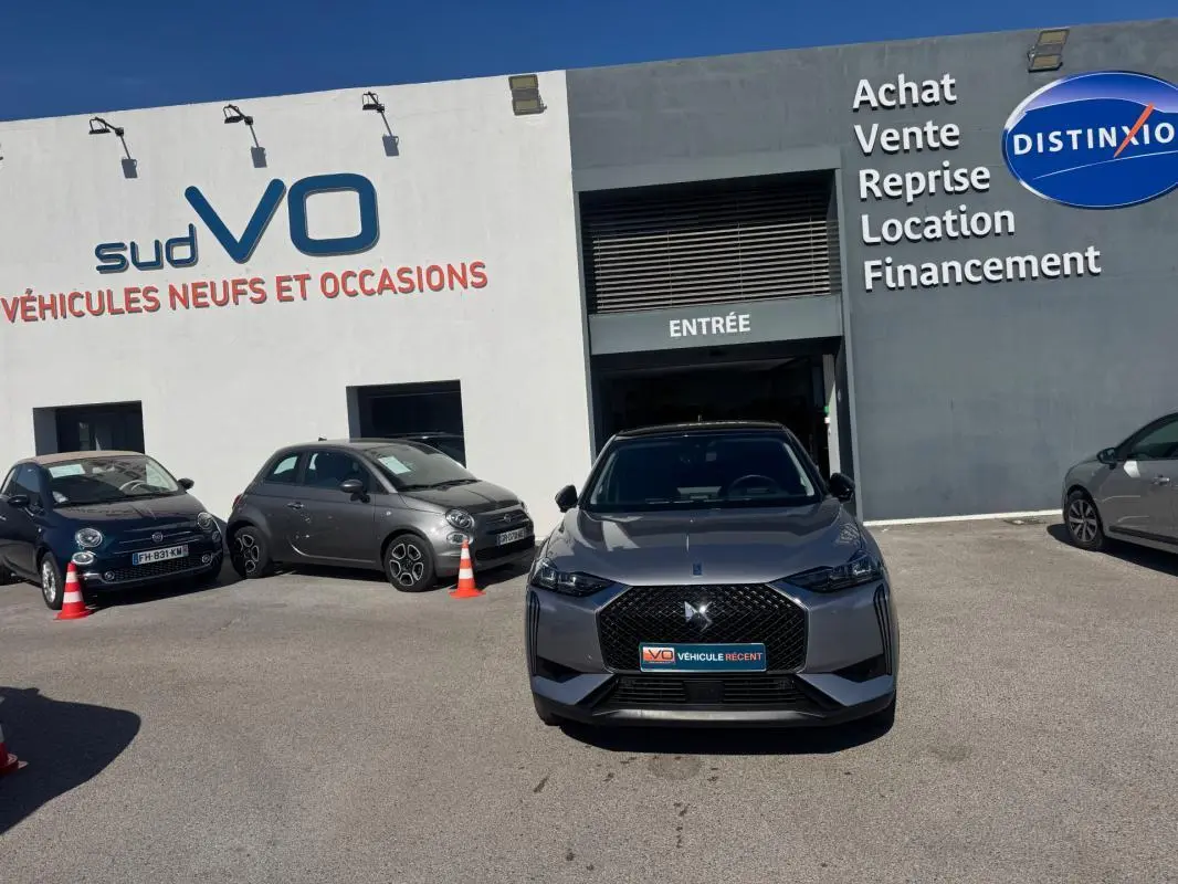 Vue de face d'une DS3 100 BVM6 Bastille gris avec calandre distinctive et jantes alliage 18 pouces, stationnée devant un garage.