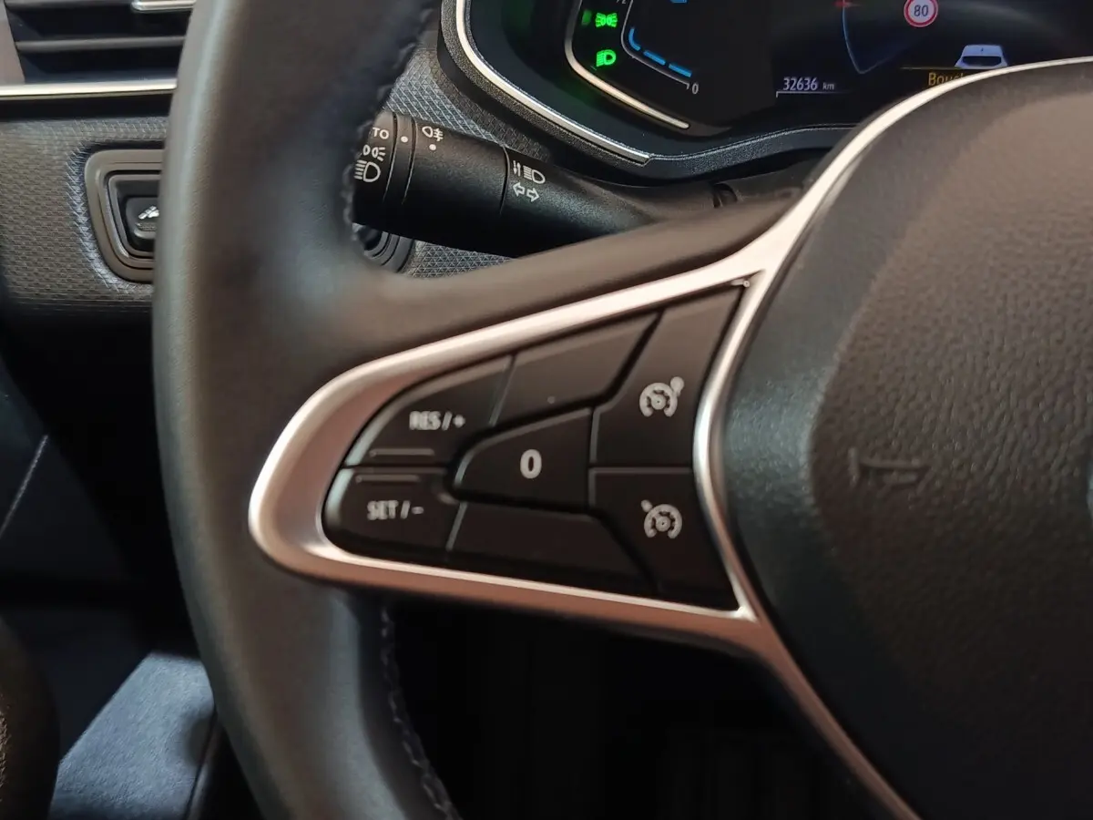 Gros plan sur les commandes du volant cuir synthétique de la Renault Clio Business E-TECH 140 blanc, affichage numérique en arrière-plan.
