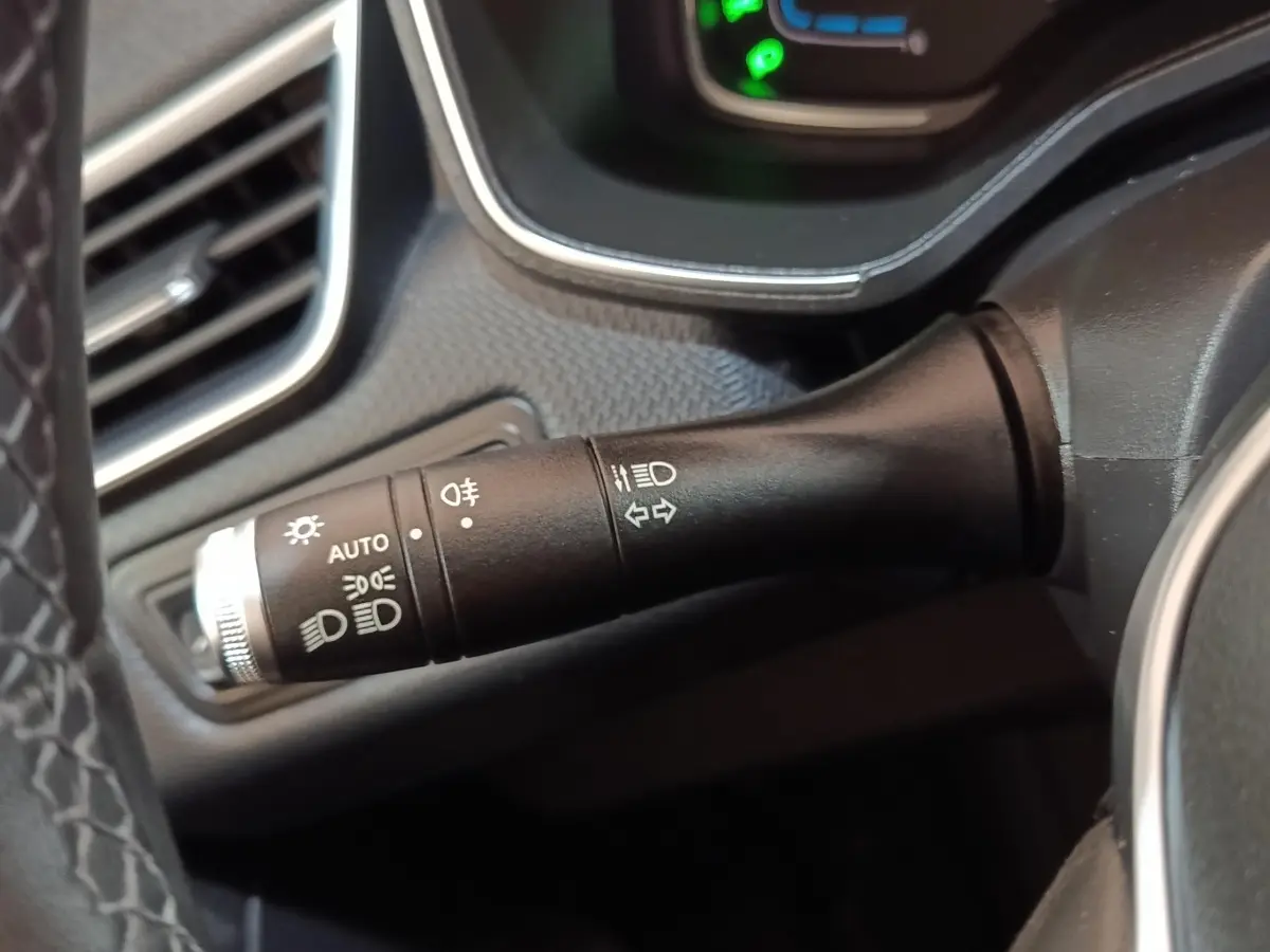 Gros plan sur la commande des phares et clignotants à gauche du volant dans l’habitacle d’une Renault Clio Business E-TECH blanche.