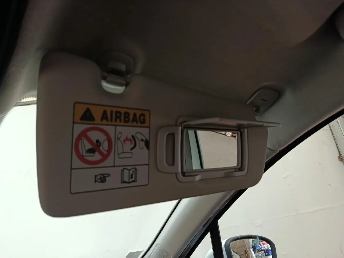 Détail intérieur du pare-soleil côté conducteur avec miroir et avertissement airbag dans une Renault Clio blanche.
