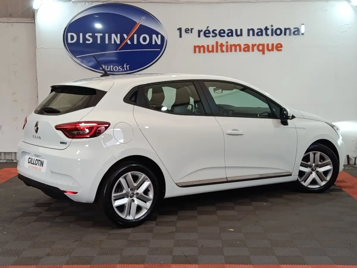 Renault Clio Business E-TECH blanc vue de profil droit en intérieur, avec jantes alliage et feux arrière LED allumés.