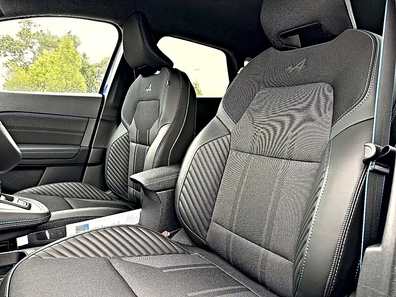 Vue intérieure des sièges avant noirs avec surpiqûres bleues et logo Alpine brodé sur les appuie-têtes du Renault Symbioz 2026.