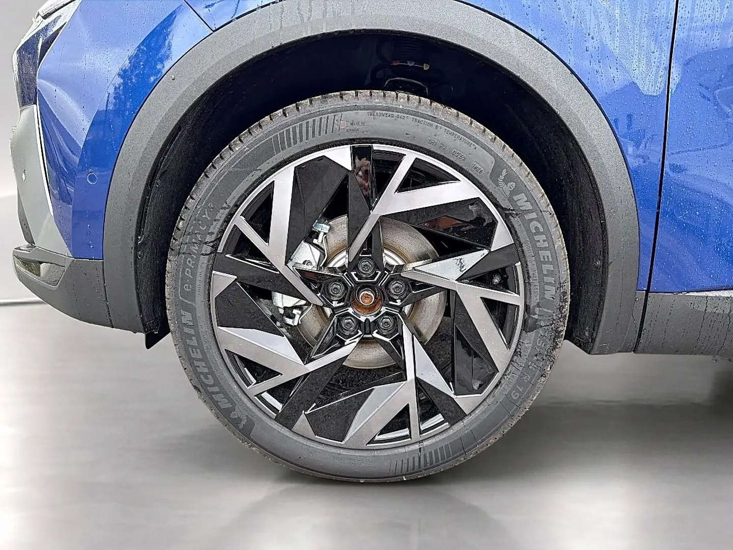 Gros plan sur la roue avant gauche avec jante alu noire et argentée du Renault Symbioz bleu iron.