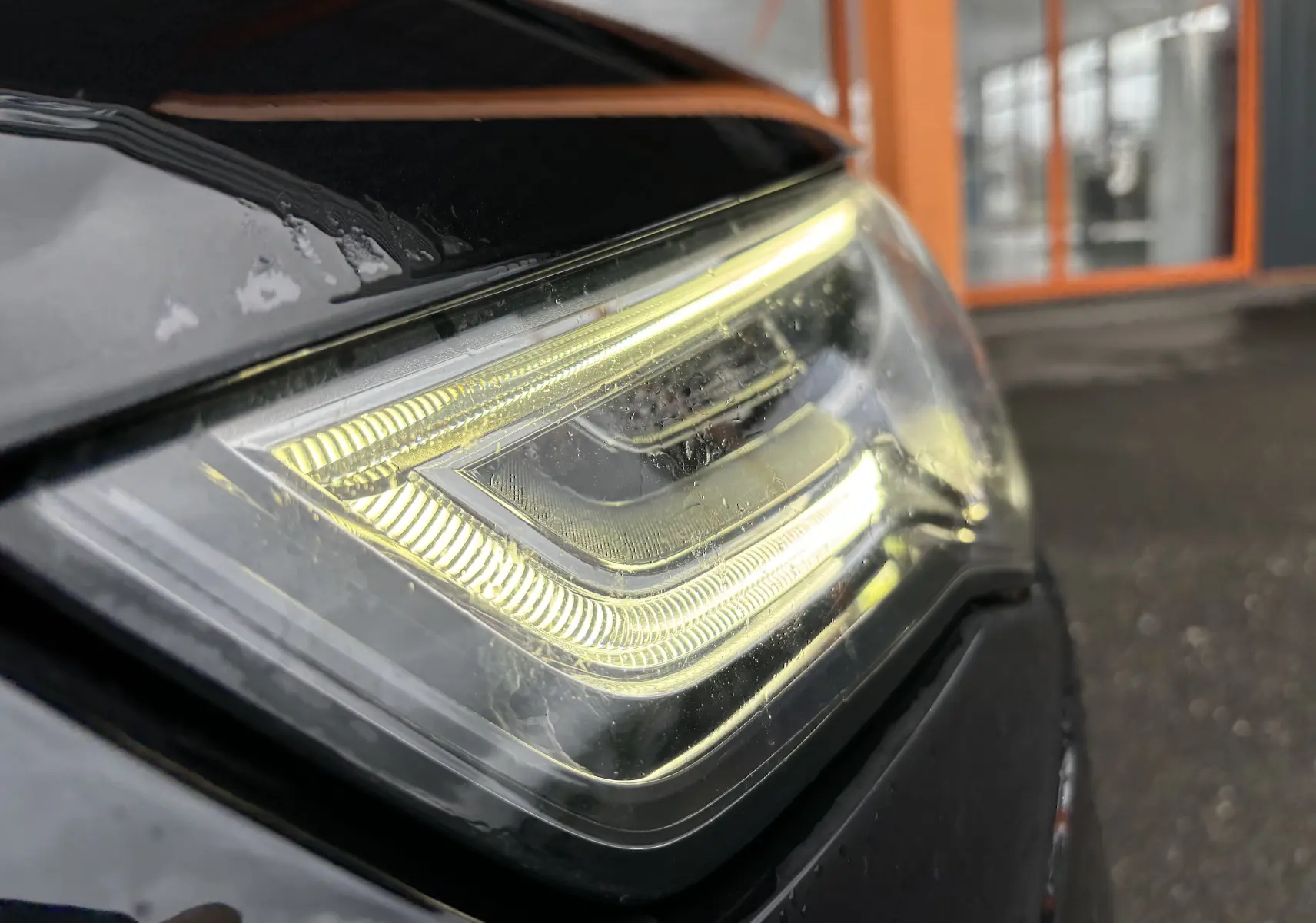 Gros plan sur le phare avant gauche allumé d'une Audi A5 Sportback noire de 2013, soulignant ses lignes LED distinctives.