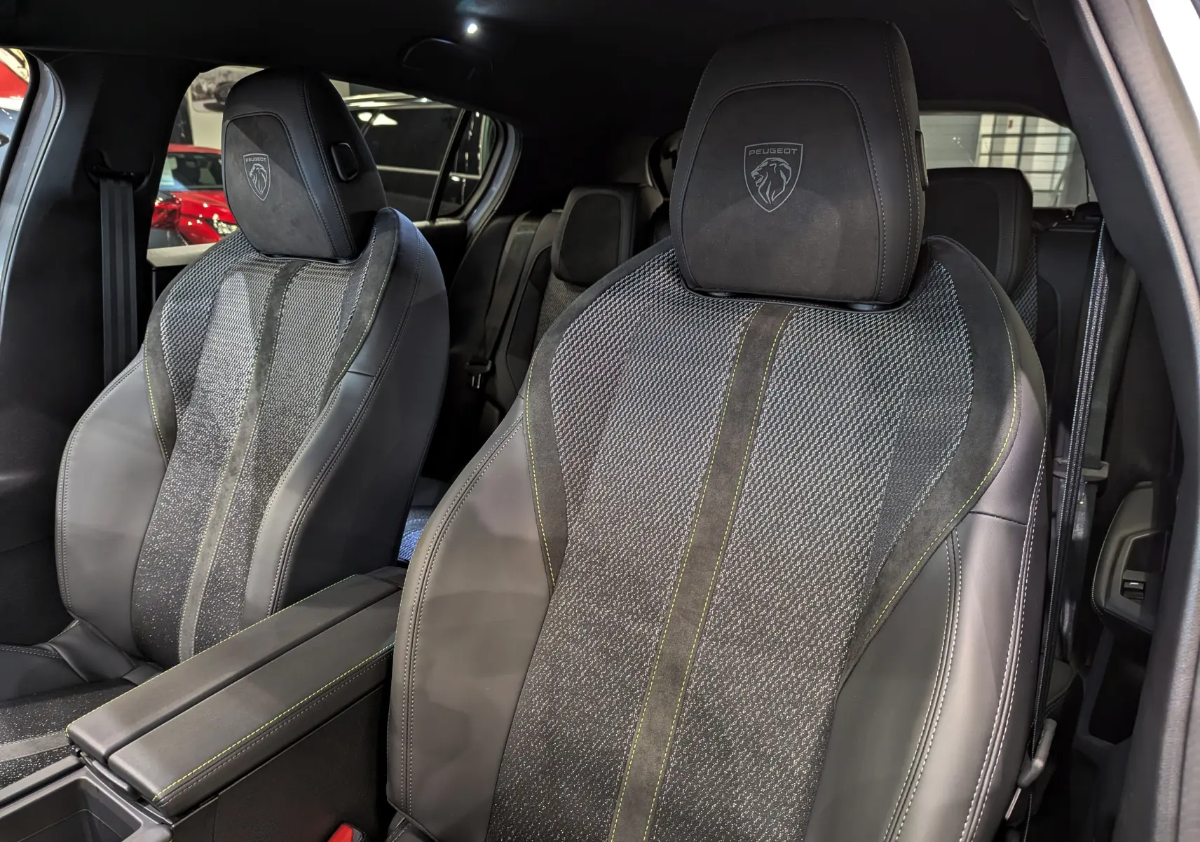 Gros plan sur les sièges avant en cuir noir et tissu gris avec logo Peugeot embossé sur appuie-tête.