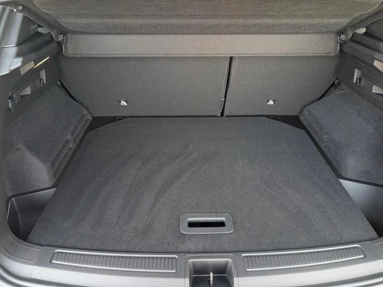 Coffre ouvert vu de l'arrière d'un Renault Austral gris métallisé, avec plancher de coffre plat et tapis noir.