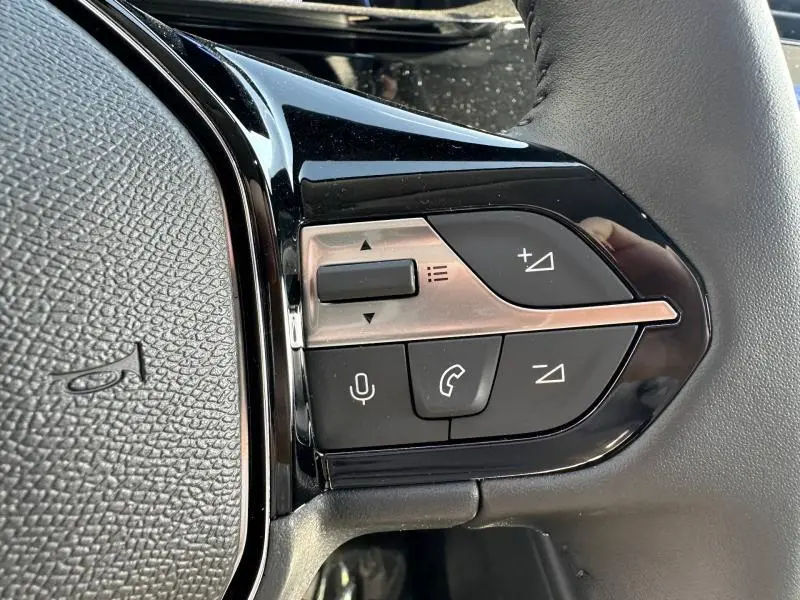 Gros plan sur les commandes multifonctions noires et argentées du volant côté gauche d'une Peugeot 308 2025.