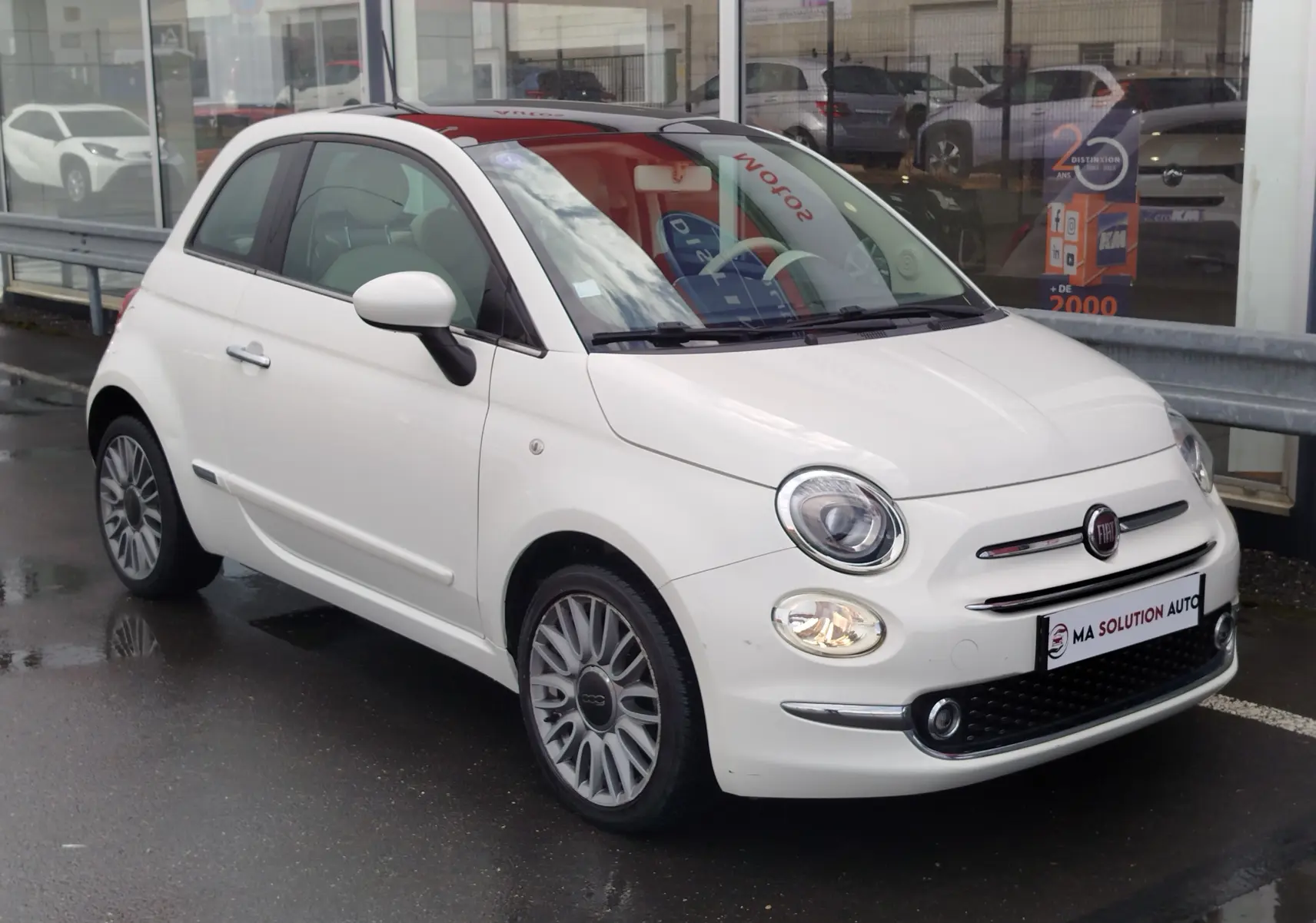 Fiat 500 Lounge blanche Bossa Nova vue 3/4 avant droit, phares allumés et jantes alliage multibranches.