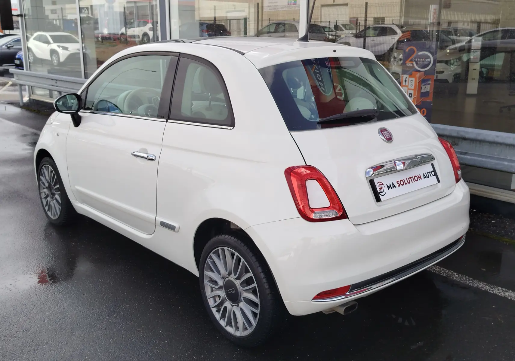 Vue 3/4 arrière droite d'une Fiat 500 blanche Bossa Nova Pastel, avec jantes alliage et feux arrière distinctifs.