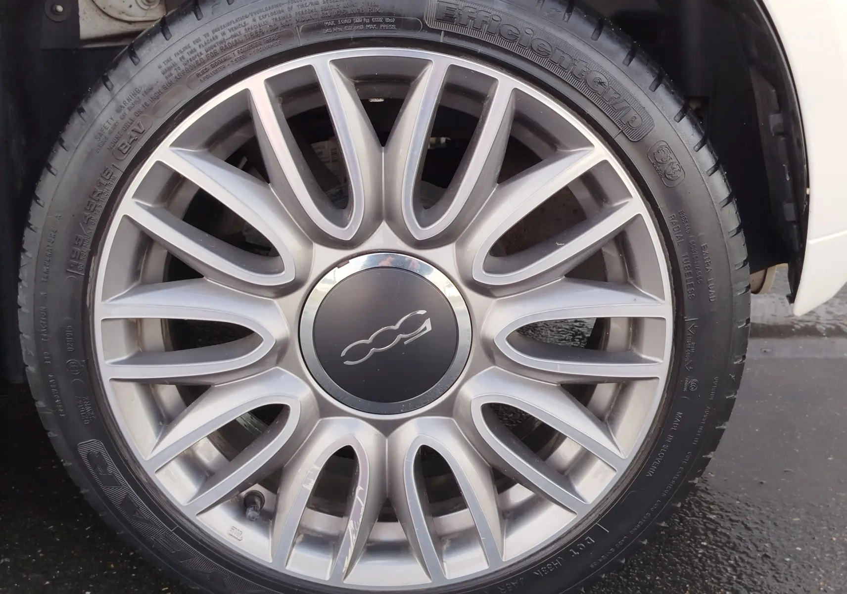 Vue rapprochée sur la roue avant gauche d'une Fiat 500 blanche Bossa Nova Pastel, montrant le passage de roue et le pneu.