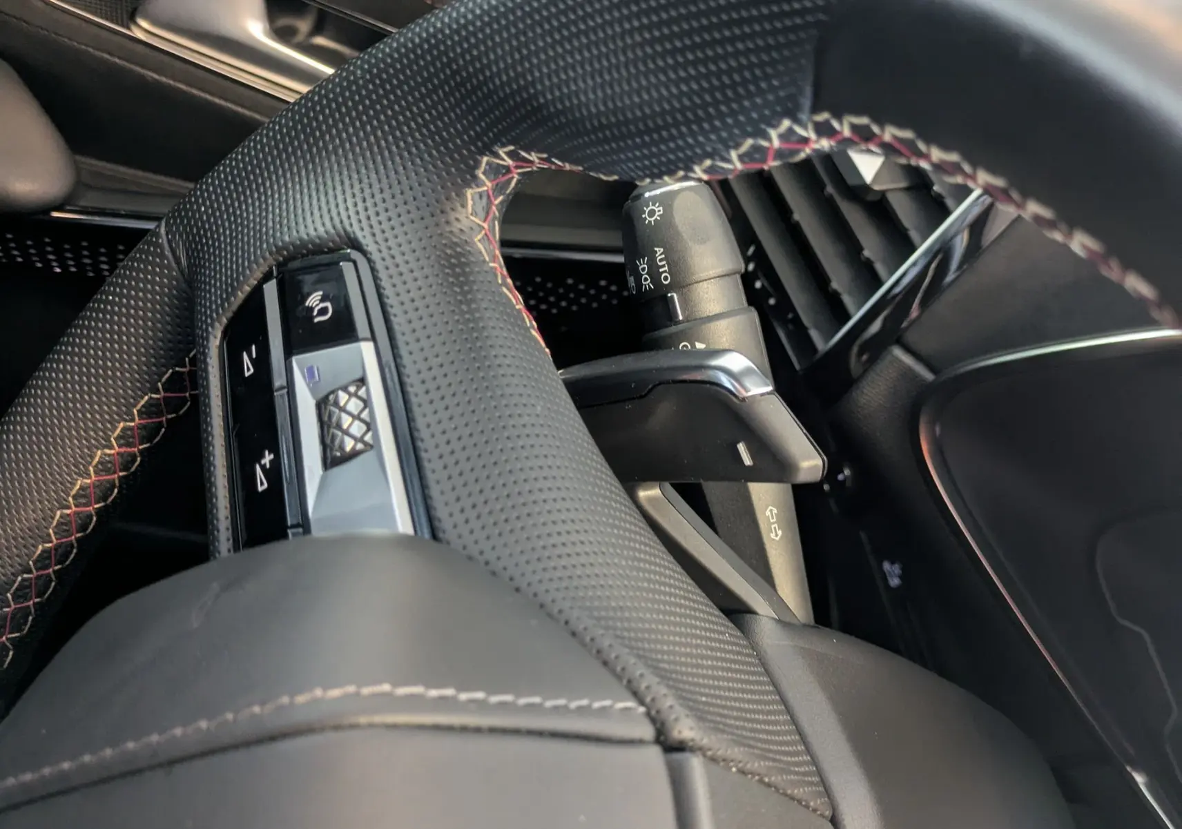 Gros plan sur le volant perforé avec surpiqûres rouges et garniture Alcantara noir du DS7 gris laqué, côté conducteur.
