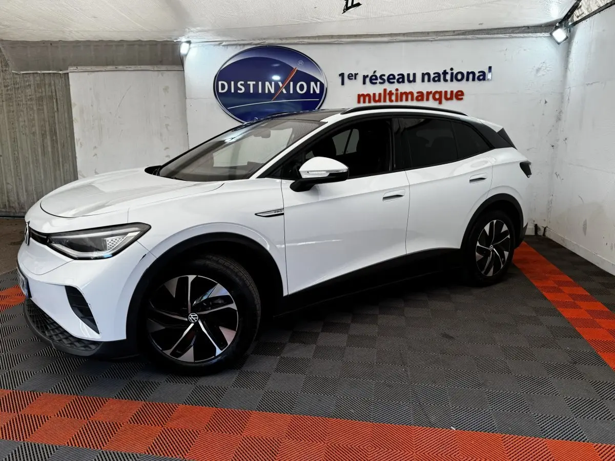Volkswagen ID.4 blanc en 3/4 avant droit, avec jantes noires et toit panoramique dans un showroom.