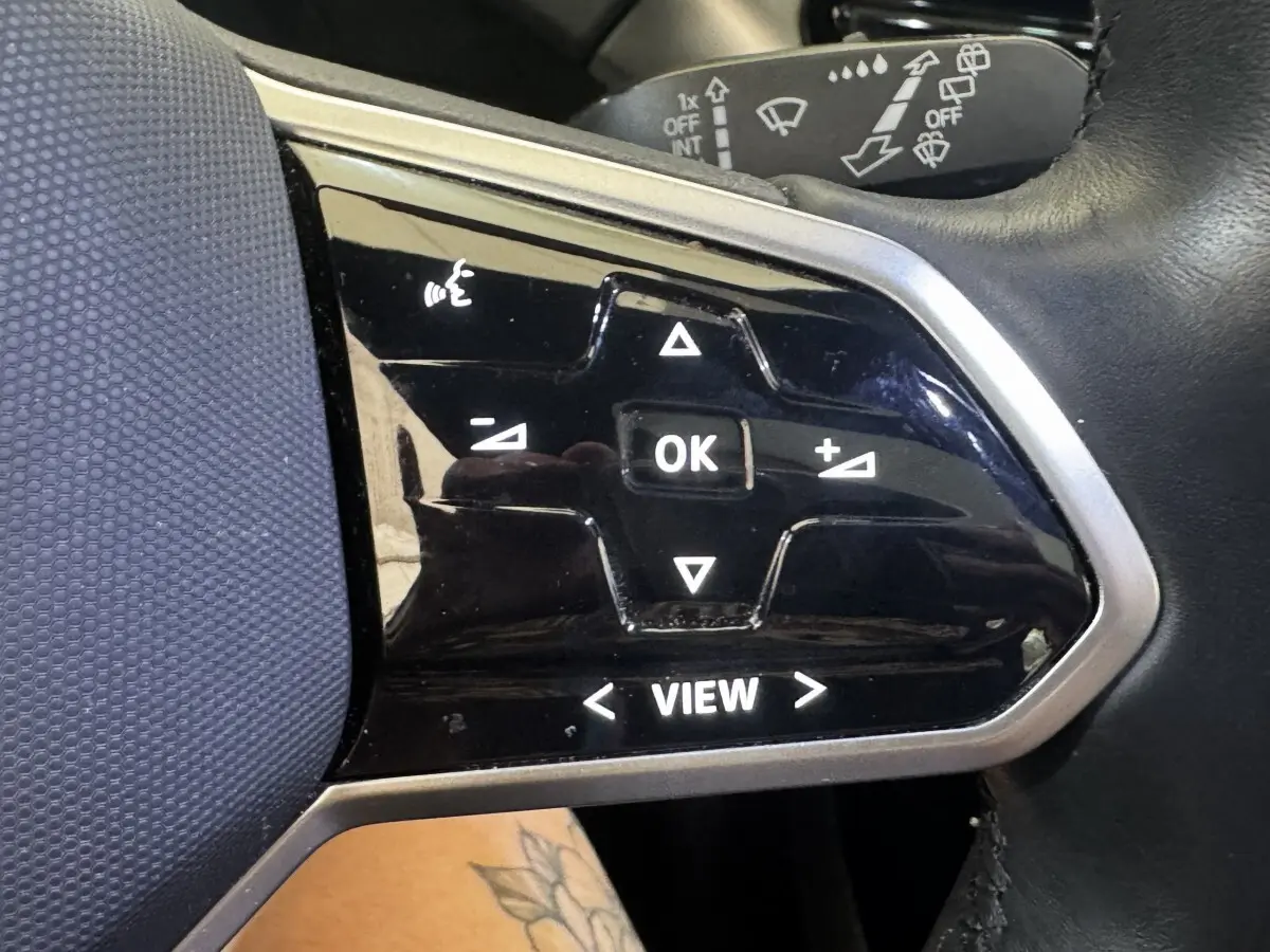 Gros plan sur les commandes noires du volant côté gauche du Volkswagen ID.4 blanc, avec boutons multifonctions éclairés.