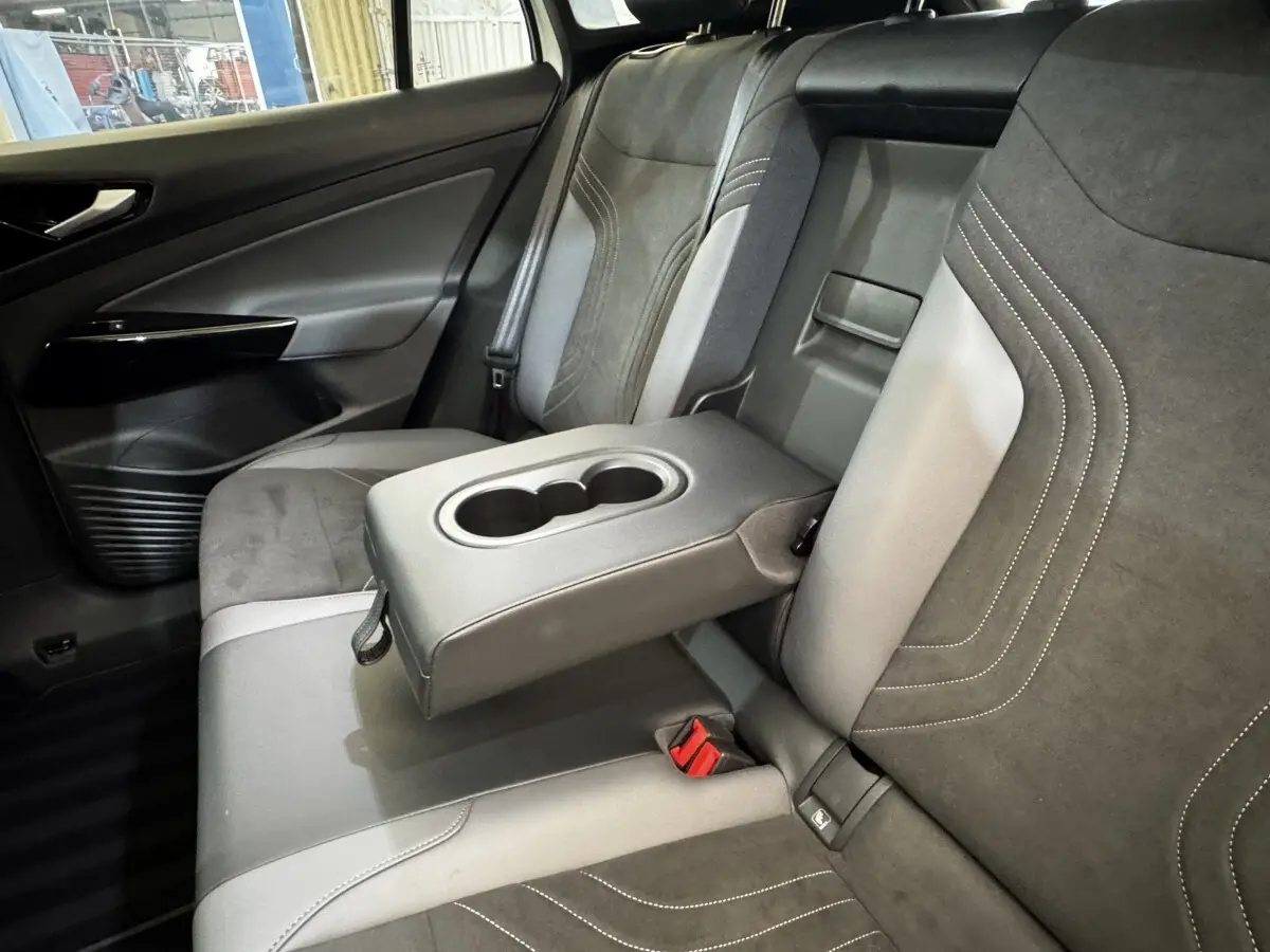 Vue intérieure côté gauche de la banquette arrière grise et noire du Volkswagen ID.4 avec accoudoir central relevé et porte-gobelets.
